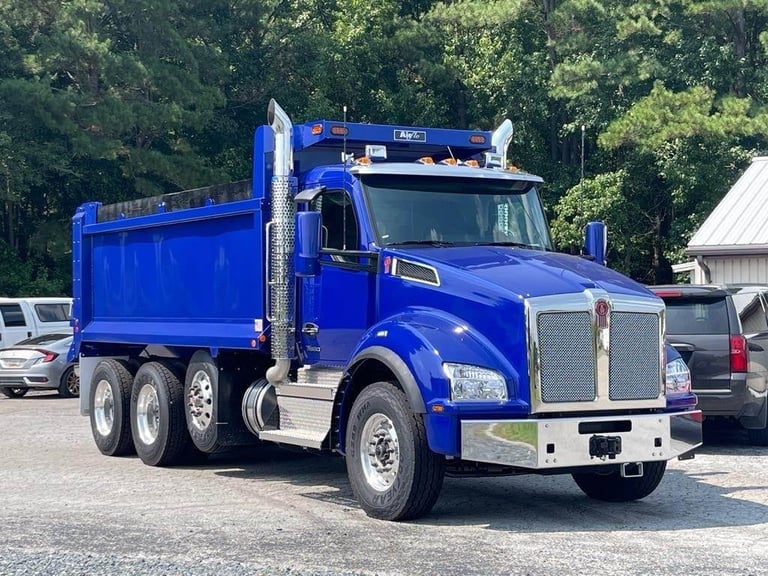 Bright blue dump truck parked in a lot with green trees in the background